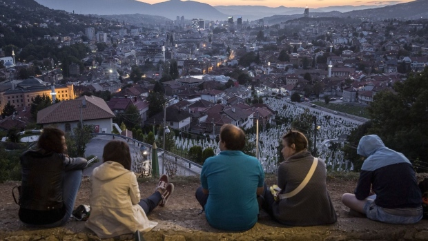 Tourists look out over a cemetery, toward commercial and residential buildings on the city skyline, in Sarajevo, Bosnia, on Monday, Sept. 10, 2018. Bosnia risks being collateral damage as world powers jostle for influence in a historical flashpoint. Balkan leaders emboldened by Russia, Turkey and Donald Trump’s revisions to U.S. foreign policy are seeking to unpick ethnic and territorial agreements that have underpinned an anxious peace for two decades. Photographer: Oliver Bunic/Bloomberg