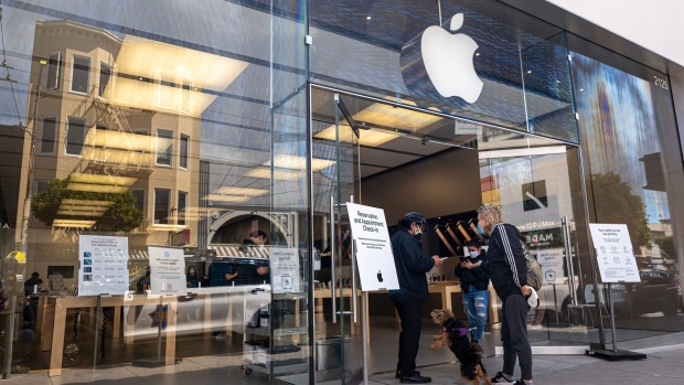 A customer wearing a protective mask waits to enter an Apple store in San Francisco, California, U.S., on Monday, April 26, 2021. Apple Inc. is increasing its U.S. investments by 20% over the next five years, allocating $430 billion to develop next-generation silicon and spur 5G wireless innovation across nine U.S. states, after outstripping its growth expectations during the pandemic.