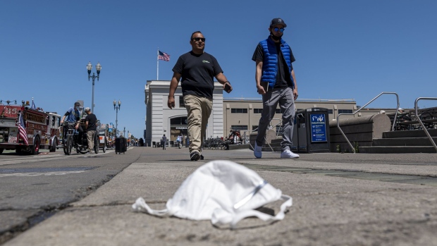 People walk past a discarded protective mask on the Embarcadero in San Francisco, California, U.S., on Tuesday, June 15, 2021. California lifted most of its Covid-19 restrictions Tuesday as part of a grand reopening in which the state will end capacity limits, physical distancing and mask requirements for those that are vaccinated.
