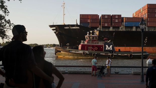 Pedestrians watch from River Street as a cargo ship and a tug boat travel into the Port of Savannah.
