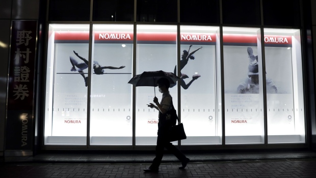 A pedestrian holding an umbrella walks past a branch of Nomura Securities Co., a unit of Nomura Holdings Inc., at night in Tokyo, Japan, on Monday, July 27, 2020. Nomura Holdings is schedule to announce first-quarter earning figures on July 29. Photographer: Kiyoshi Ota/Bloomberg