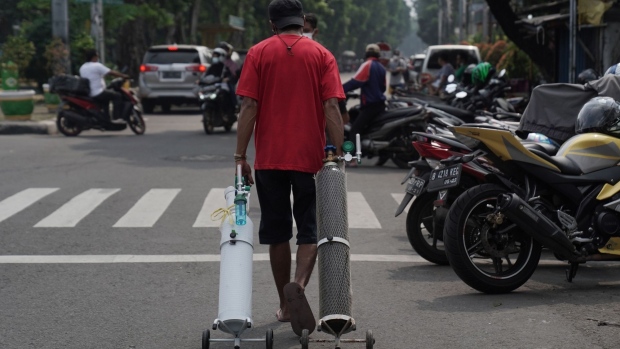 A man carries oxygen bottles after refilling them at a refill station in Jakarta, Indonesia, on Monday, July 5, 2021. Indonesia tightened entry requirements for travelers and ordered a ramp-up in oxygen production as the nation saw its worst day for Covid-19 deaths.