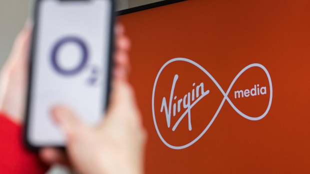 The 02 logo, of Telfonica SA's U.K. unit, sits on a mobile phone held in front of a Virgin Media logo, a unit of Liberty Global Plc, on a television in this arranged photograph near Guilford, U.K., on Monday, May 4, 2020. Telefonica and John Malone's Liberty Global have never been closer to finally creating the U.K.'s biggest telecom operator after flirting with various combinations over the years. Photographer: Jason Alden/Bloomberg