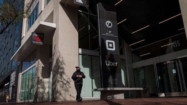 A pedestrian wearing a protective mask passes in front of signage displayed outside Uber Technologies headquarters in San Francisco, California, U.S., on Monday, May 4, 2020. Lyft Inc. withdrew its profit and revenue forecasts for 2020, following rival Uber Technologies Inc. in citing evolving and unpredictable impacts from Covid-19. Photographer: David Paul Morris/Bloomberg