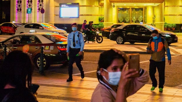 People wearing protective masks walk in front of the Casino Lisboa, operated by SJM Holdings Ltd., at night in Macau, China, on Tuesday, March 3, 2020. Casinos in Macau, the Chinese territory that's the worlds biggest gambling hub, reported a record drop in gaming revenue, as they grappled with the cost of closing down their businesses for 15 days to help contain the deadly coronavirus outbreak.