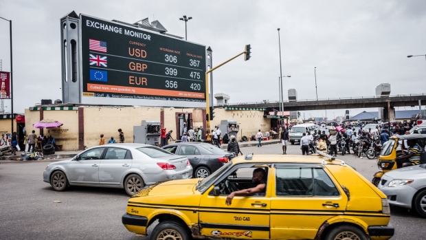 A taxi cab passes a giant advertising screen showing US dollar, British pound and euro foreign currency exchange rates on a busy city road in Lagos, Nigeria, on Wednesday, July 26, 2017. Nigeria's economy, which in 2016 suffered its first full-year recession since 1987, will probably return to growth in 2017. Photographer: Tom Saater/Bloomberg