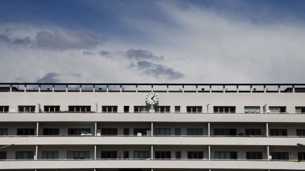 A clock and balcony walkways on the Bridge House at the White City modernist residential apartment housing estate, a UNESCO World Heritage site managed by Deutsche Wohnen SE, in Berlin, Germany, on Tuesday, May 25, 2021. German residential property firm Vonovia SE agreed to acquire rival Deutsche Wohnen for about 19 billion euros ($23 billion) in the biggest-ever takeover in European real estate, a deal that risks further stoking tensions over affordable housing. Photographer: Liesa Johannssen-Koppitz/Bloomberg
