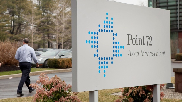 Employees walk past signage displayed outside of Point72 Asset Management LP in Stamford, Connecticut.