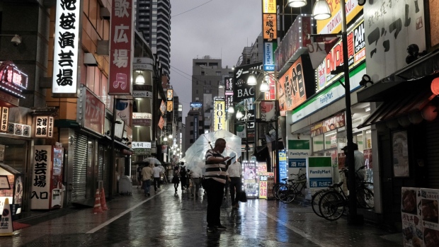 A pedestrian looks at a phone near izakaya bars at dusk in the Ikebukuro district in Tokyo, Japan, on Friday, Aug. 13, 2021. The spread of the virus in Tokyo is at disaster levels comparable with the heavy rains and flooding hitting Japan's west and residents should stay at home and get vaccinated, Tokyo’s governor warned a day after an expert adviser said the virus was out of control. Photographer: Soichiro Koriyama/Bloomberg