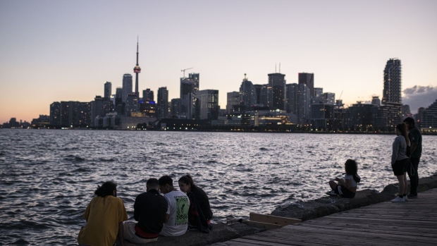 People sit on a dock along the skyline during sunset in Toronto, Ontario, Canada, on Saturday, June 19, 2021. Ontario is now allowing limited outdoor dining and public gatherings, after the province cleared the vaccination threshold required to move into its first stage of reopening. Photographer: Christopher Katsarov Luna/Bloomberg