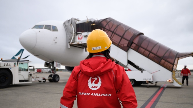 A ground crew member stands in front of a Boeing 767-300ER aircraft operated by Japan Airlines Co. (JAL) at Narita Airport in Narita, Japan, on Saturday, Sept. 26, 2020. JAL operated a 3.5-hour sightseeing flight, which offer passengers scenic views of the sunset and star-lit sky, on Saturday making use of an idling aircraft because of fight reductions amid the coronavirus pandemic. Photographer: Akio Kon/Bloomberg