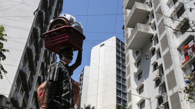A pedestrian carrying pots and pans on his head walks past residential buildings in Mumbai, India, on Saturday, Feb 6, 2021. India's central bank kept interest rates on hold Friday and began withdrawing some pandemic-era policies, while reiterating its intent to keep its stance accommodative to support economic growth.