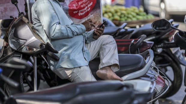 A man uses a smartphone while sitting on a motorcycle in Mumbai, India, on Saturday, Feb. 15, 2020. Facebook, YouTube, Twitter and TikTok will have to reveal users' identities if Indian government agencies ask them to, according to the country’s controversial new rules for social media companies and messaging apps expected to be published later this month. Photographer: Dhiraj Singh/Bloomberg