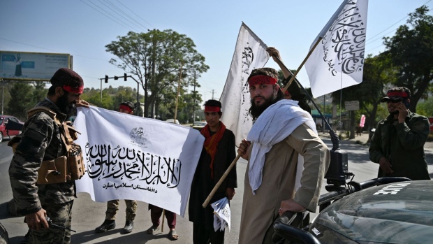 Taliban fighters hold Taliban flags while standing guard along a road in Kabul Photographer: Wakil Kohsar/AFP/Getty Images