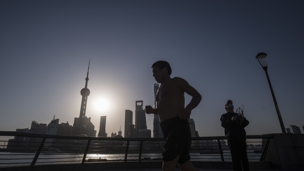 A runner jogs past a man flying a kite on the Bund as skyscrapers of the Pudong Lujiazui Financial District stand across the Huangpu River during sunrise in Shanghai, China, on Friday, March 20, 2020. Most of China is now considered low risk and should return to normal work and life, Premier Li Keqiang said at a government meeting on the coronavirus, which is spreading rapidly in Europe, the U.S. and elsewhere.