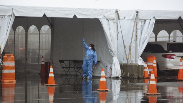 A health care worker in a protective suit gestures inside a six lane COVID-19 drive-through testing facility at Glen Island Park in New Rochelle, New York, U.S., on Friday, March 13, 2020. President Donald Trump plans to declare a national emergency on Friday over the coronavirus outbreak, invoking the Stafford Act to open the door to more federal aid for states and municipalities, according to two people familiar with the matter. Photographer: Angus Mordant/Bloomberg