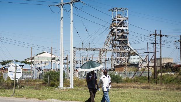 Pedestrians walk down the road as the Impala Platinum Holdings Ltd., also known as Implats, shaft 2 mine tore stands beyond in Rustenburg, South Africa, on Wednesday, April 22, 2020. South Africa allowed mining companies to resume operations at half their normal capacity as the government takes its first steps to ease a nationwide coronavirus lockdown. Photographer: Waldo Swiegers/Bloomberg