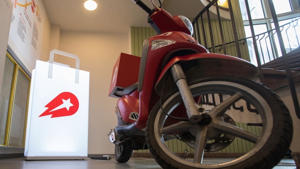 An illuminated bag-shaped logo and a delivery moped motorcycle stand in the reception area of the Delivery Hero AG headquarter offices in Berlin, Germany.