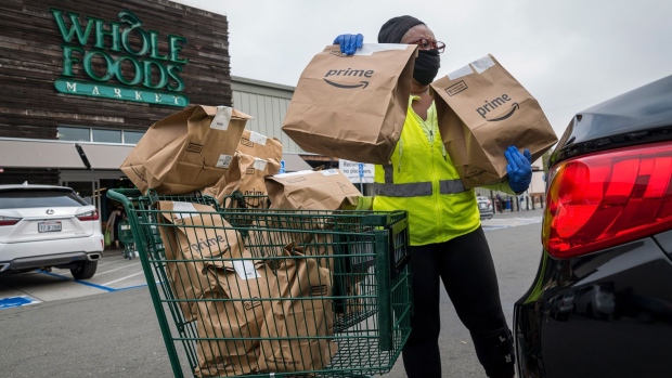 An independent contractor wearing a protective mask and gloves loads Amazon Prime grocery bags into a car outside a Whole Foods Market in Berkeley, California.