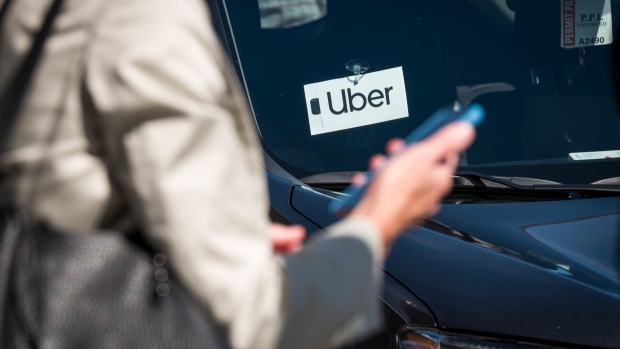 A traveler uses a smartphone in front of a vehicle displaying Uber Technologies Inc. signage at the Oakland International Airport in Oakland, California, U.S., on Tuesday, Aug. 6, 2019. Uber Technologies Inc. is scheduled to release earnings figures on August 8. Photographer: David Paul Morris/Bloomberg