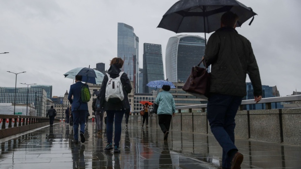 Commuters use their umbrellas to shelter from the rain as they cross London Bridge in London, U.K., on Monday, June 21, 2021. Almost half of London companies whose staff can work from home expect them to do so up to five days a week after the pandemic finishes, and smaller businesses are more likely than larger ones to move ahead with remote working. Photographer: Hollie Adams/Bloomberg