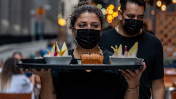 A worker wears a protective mask while carrying a tray with food in the outside dining area of Crown Shy restaurant in New York, U.S., on Saturday, Sept. 26, 2020. New York City currently prohibits all indoor dining, but will allow restaurants to open indoor dining rooms at 25% capacity, beginning September 30.