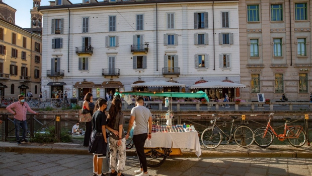 Pedestrians stop by a street vendor's stall in the Navigli neighborhood in Milan, Italy, on Thursday, May 27, 2021. Italy has approved a 40-billion-euro ($49 billion) stimulus package that extends economic support for businesses and families hurt by Covid-19 restrictions. Photographer: Francesca Volpi/Bloomberg