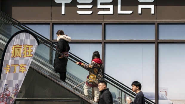 Shoppers ride an escalator in front of the Tesla Inc. showroom at the Chamtime Plaza in Shanghai, China, on Monday, March 8, 2021. China's electric-car makers are paying top-dollar rents to open showrooms in luxury malls, as they seek to gain an edge in the hyper-competitive market. Photographer: Qilai Shen/Bloomberg