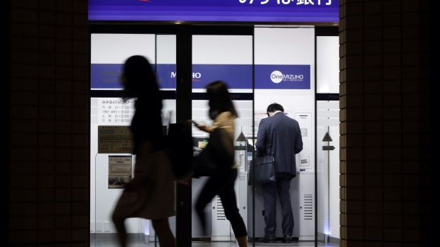Pedestrians walk past a customer using an automated teller machine (ATM) at a branch of Mizuho Bank Ltd., a unit of Mizuho Financial Group Inc. (MHFG), at night in Tokyo, Japan, on Wednesday, May 13, 2020. Japan’s biggest banks are expected to project the highest bad-loan costs in a decade when they issue annual profit forecasts this week, joining global peers in bracing for the worst global recession since the Great Depression.