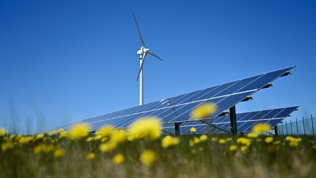 A wind turbine and solar panels in a field of yellow flowers. Photographer: Mikael Sjoberg/Bloomberg