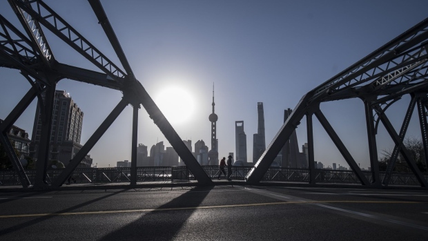 Pedestrians walks across a bridge as skyscrapers of the Pudong Lujiazui Financial District stand across the Huangpu River during sunrise in Shanghai, China, on Friday, March 20, 2020. Most of China is now considered low risk and should return to normal work and life, Premier Li Keqiang said at a government meeting on the coronavirus, which is spreading rapidly in Europe, the U.S. and elsewhere. Photographer: Qilai Shen/Bloomberg