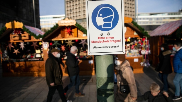 A sign advises pedestrians to wear a mask at a Christmas market on Kurfrstendamm, in Berlin, Germany, on Friday, Nov. 26, 2021. Chancellor Angela Merkel said the latest surge in Covid-19 infections is worse than anything Germany has experienced so far and called for tighter restrictions to help check the spread.