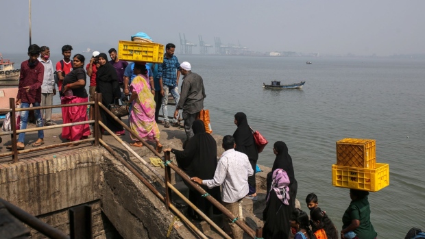 Passengers disembark from a boat as gantry cranes at the Jawaharlal Nehru Port in the distance in Navi Mumbai, Maharashtra, India, on Sunday, Nov. 14, 2021. Congestion at many of the world’s major ports offered a snapshot of supply chains trying to avoid unprecedented bottlenecks, as cargo handlers searched for the quickest way to route goods through the clogged arteries of global commerce.