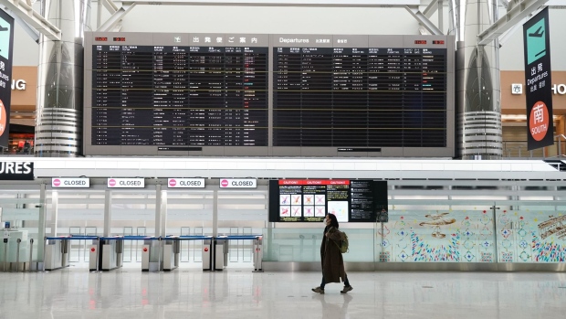 A woman wearing a protective mask walks past a flight information board in a departure hall at Narita Airport in Narita, Chiba Prefecture, Japan, on Tuesday, Nov. 30, 2021. Japan closed its borders to new foreign arrivals from Tuesday and have its own citizens isolate on arrival from countries where the omicron variant has been found, while experts around the world analyze the risks it presents.