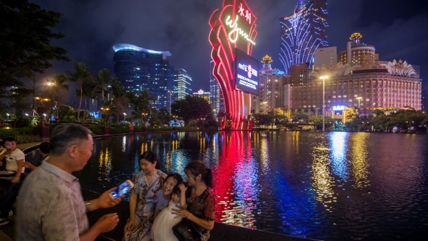 The Wynn Resorts Ltd. logo stands illuminated as people sit by the fountain at the Wynn Macau casino resort in Macau, China, on Tuesday, July 24, 2018. Earnings from Macau casino operators are expected to remain healthy for the second quarter, though concerns are increasing over a slowing China economy and a weaker showing by high-stakes gamblers.