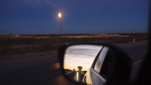 A gas flare burns as a truck is seen in the rearview mirror of a car in the Permian Basin area of Loving County, Texas.