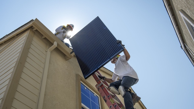 Contractors move a SunRun Inc. solar panel up a ladder to the roof of a new home at the Westline Homes Willowood Cottages community in Sacramento, California.