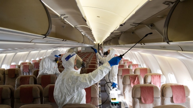 Workers wearing personal protective equipment (PPE) spray disinfectant inside an Asiana Airlines Inc. aircraft at Incheon International Airport in Incheon, South Korea, on Thursday, Dec. 9, 2021. The South Korean won advances for a third day, with risk appetite supported by a report saying three vaccine doses could neutralize the omicron variant.