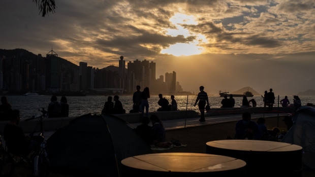 Pedestrians walk along a promenade during sunset in Hong Kong, China, on Tuesday, Dec. 7, 2021. Hong Kong will prioritize quarantine-free travel for business people when its China border reopens, Chief Executive Carrie Lam said, warning that the city’s vaccination rate could curb a broader roll-out. Photographer: Paul Yeung/Bloomberg