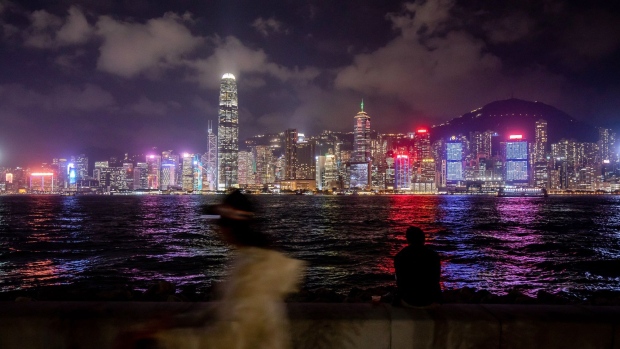 A pedestrian walks along a promenade in front of the city's skyline in Hong Kong, China, on Tuesday, Dec. 7, 2021. Hong Kong will prioritize quarantine-free travel for business people when its China border reopens, Chief Executive Carrie Lam said, warning that the city’s vaccination rate could curb a broader roll-out.