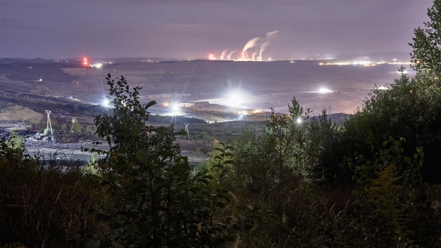 Lights illuminate an open pit lignite mine near emissions rising from chimneys at the Turow coal powered power plant in Bogatynia, Poland.