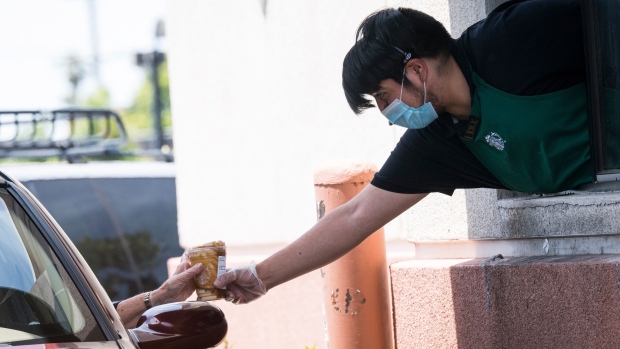 A Starbucks Corp. employee wearing protective gloves and a mask hands a beverage to a customer through a drive-thru window at a store in El Cerrito, California, U.S., on Wednesday, June 10, 2020. Starbucks Corp. expects the coronavirus pandemic to reduce sales this quarter by as much as $3.2 billion, dragging down the coffee chains performance as it sees a recovery stretching into next year.