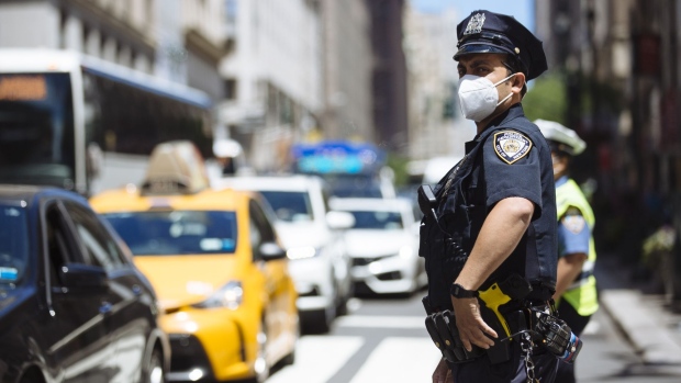 A New York City Police Department (NYPD) officer wearing a protective mask directs traffic in the Midtown neighborhood of New York, U.S., on Wednesday, June 17, 2020. With two weeks to get City Council approval of a spending plan that plugs a $9 billion revenue gap in the next two years, Mayor Bill de Blasio faces renewed calls to slash more than $1 billion from the NYPD.