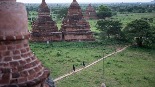 Visitors walk down a path between Buddhist temples and pagodas in Bagan, Myanmar, on Saturday, June 10, 2017. When the country opened to the outside world in 2011 after decades of military rule, the former British colony held promise as one of the world’s hottest tourist destinations, a last frontier for adventure travel. But it hasn't worked out that way. A construction glut has flooded Myanmar with unused hotel rooms, and poorly regulated building has damaged national treasures like the archaeological site of Bagan. Photographer: Taylor Weidman/Bloomberg