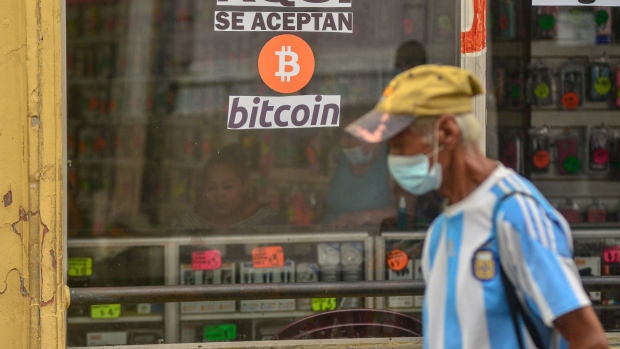 A pedestrian walks by a cellphone accessories shop that accepts Bitcoin in the Historical Center of San Salvador, El Salvador, on Thursday, Sept. 30, 2021. The government's new digital wallet, called Chivo, was designed to facilitate Bitcoin transactions, but the ease with which users can top up their balances and switch instantly between dollars and tiny, fractional amounts of the cryptocurrency makes it a perfect tool for speculation.