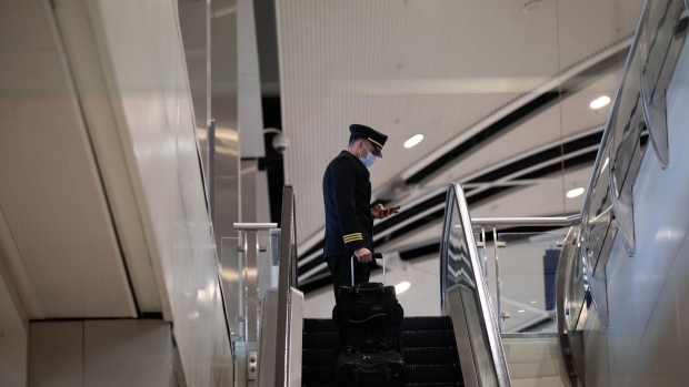 A pilot rides an escalator at the Detroit Metropolitan Wayne County Airport in Romulus, Michigan, U.S., on Wednesday, Dec. 22, 2021. Airline passenger numbers in the U.S. totaled 1.98 million on Dec. 21, compared with 992,167 the same weekday a year earlier, according to the Transportation Security Administration. Photographer: Emily Elconin/Bloomberg