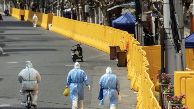 Workers wearing personal protective equipment (PPE) walk past a perimeter wall of a neighborhood under lockdown due to Covid-19 in Shanghai, China, on Wednesday, March 30, 2022. Shanghai's lockdown will have even greater ramifications for China and the world than the already significant impact from the lockdown in the tech hub of Shenzhen, according to Bloomberg Intelligence. Photographer: Qilai Shen/Bloomberg