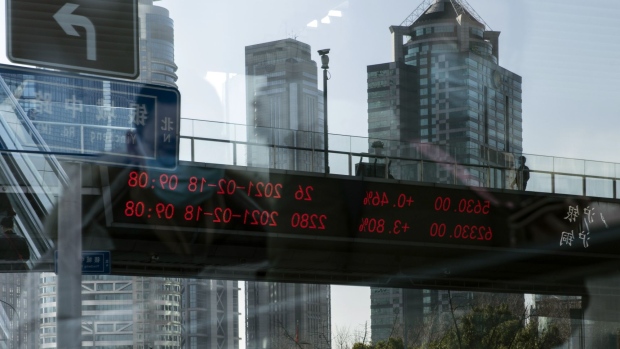 A pedestrian walks along an elevated walkway and an electronic ticker displaying stock figures are reflected in a pane of glass in Pudong's Lujiazui Financial District in Shanghai, China, on Thursday, Feb. 18, 2021. China's stock benchmark erased gains after briefly surpassing its 2007 closing peak, as mainland financial markets opened for the first time following the Lunar New Year break. Photographer: Qilai Shen/Bloomberg