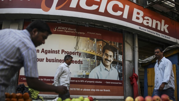 A roadside vendor arranges fruits at a stall as pedestrians walk past a ICICI Bank Ltd. branch in Mumbai, India, on Friday, Jan. 27, 2017. While economists urge more investment in roads, ports and railways when the Indian government presents its budget Feb. 1, and maybe even direct cash transfers to boost consumption, a splurge carries the risk of a rating downgrade.