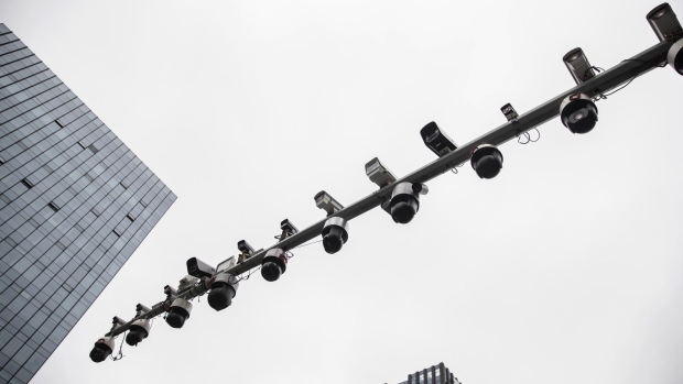 A pedestrian walks across a road past surveillance cameras manufactured by Hangzhou Hikvision Digital Technology Co. mounted on a post at a testing station near the company's headquarters in Hangzhou, China, on Tuesday, May 28, 2019. Hikvision, which is controlled by the Chinese government, is one of the leaders in the market for surveillance technology, with cameras that can produce sharp, full-color images in fog and near-total darkness.